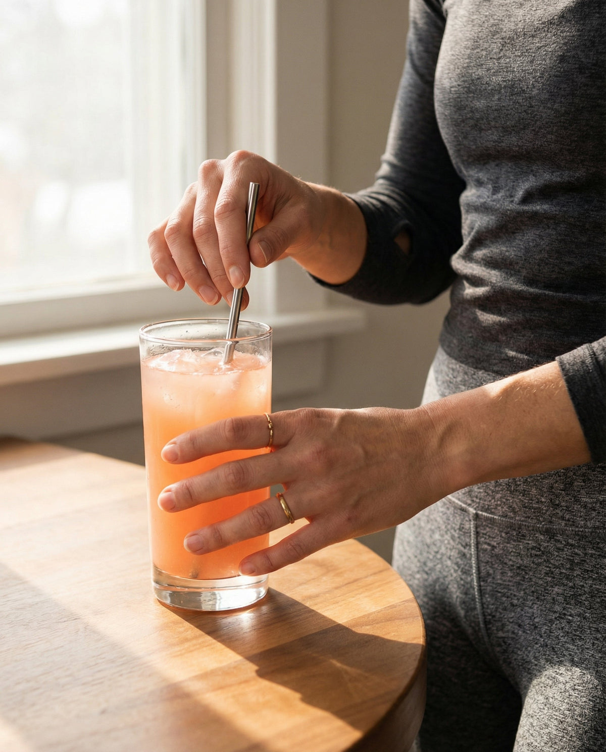 Frau rührt einen frischen Morgen-Drink mit Metallstrohhalm – natürliche Ayurveda-Routine, um den Stoffwechsel am Morgen zu aktivieren